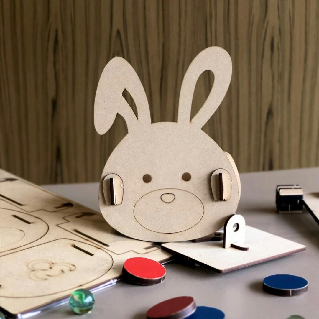 A wooden bunny-shaped craft assembled from pieces on a table, surrounded by colored chips and a wood panel backdrop.