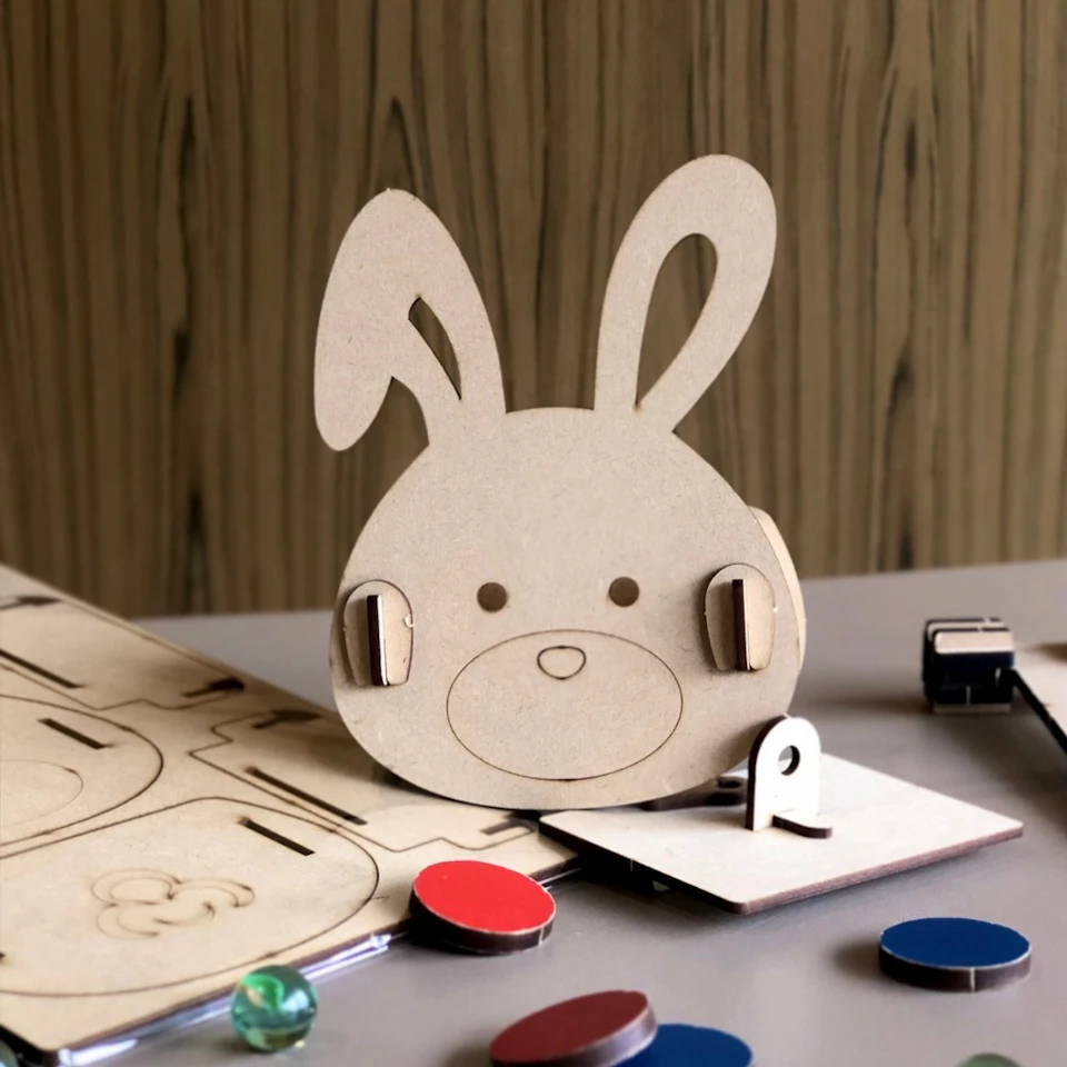 A wooden bunny-shaped craft assembled from pieces on a table, surrounded by colored chips and a wood panel backdrop.