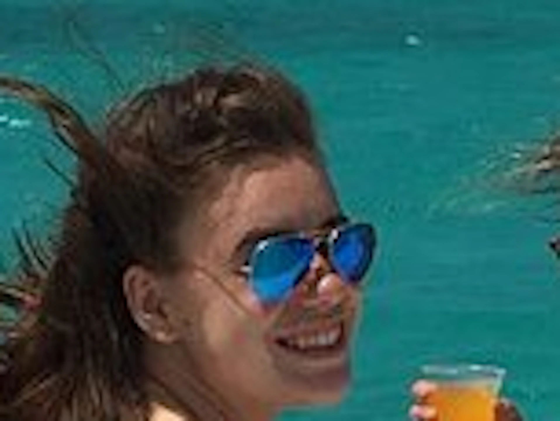 A group of women in swimsuits enjoy drinks on a boat, with turquoise ocean and blue sky in the background.