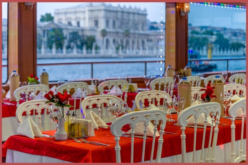 优雅的餐厅，配有红色桌布、白色椅子和摆放整齐的桌子，靠近窗户，可俯瞰历史悠久的海滨建筑。