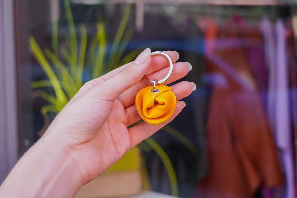 A hand holding a keychain with a yellow fabric flower against a blurred, colorful background.