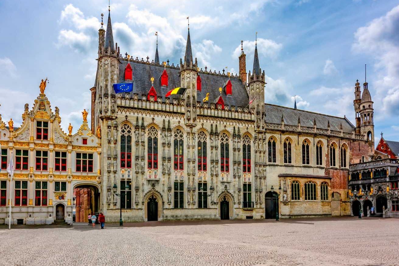 哥特式建筑，饰有华丽的细节、尖顶和旗帜。 毗邻的拱门。前景中的鹅卵石广场。 左边的人。