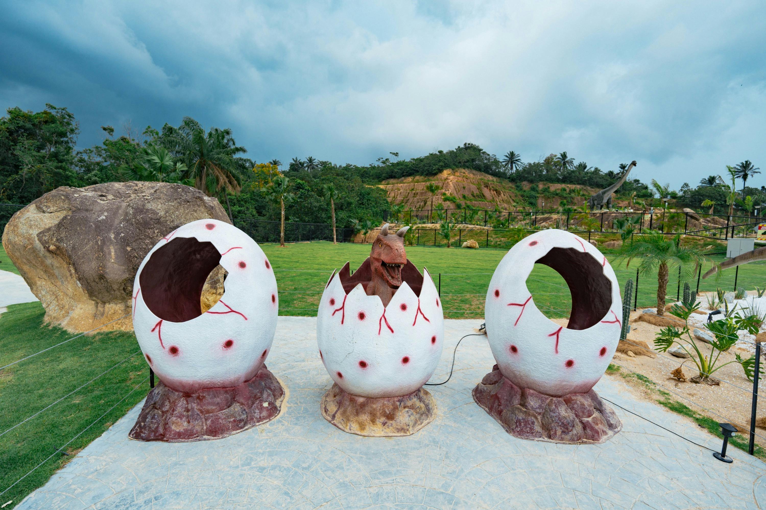 Three large decorative dinosaur eggs on a natural-themed display, with one egg showing a dinosaur hatching.