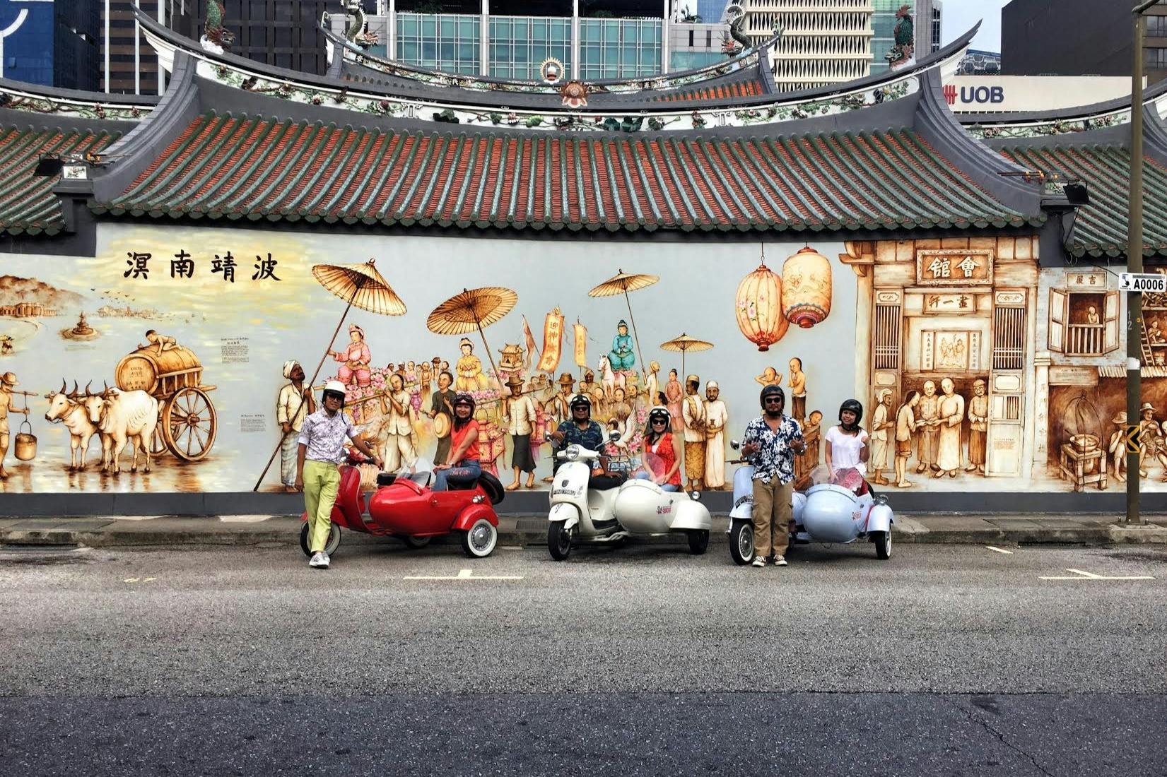 Des personnes avec des scooters décoratifs posent devant une peinture murale colorée représentant une scène historique, sur fond urbain.