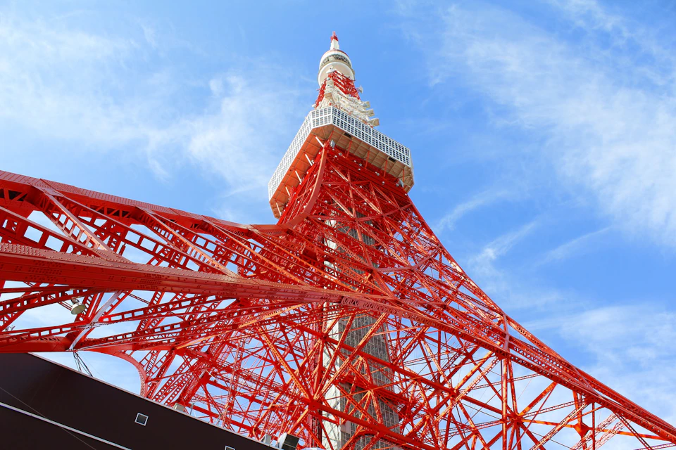 Red steel lattice tower against a blue sky with white clouds.