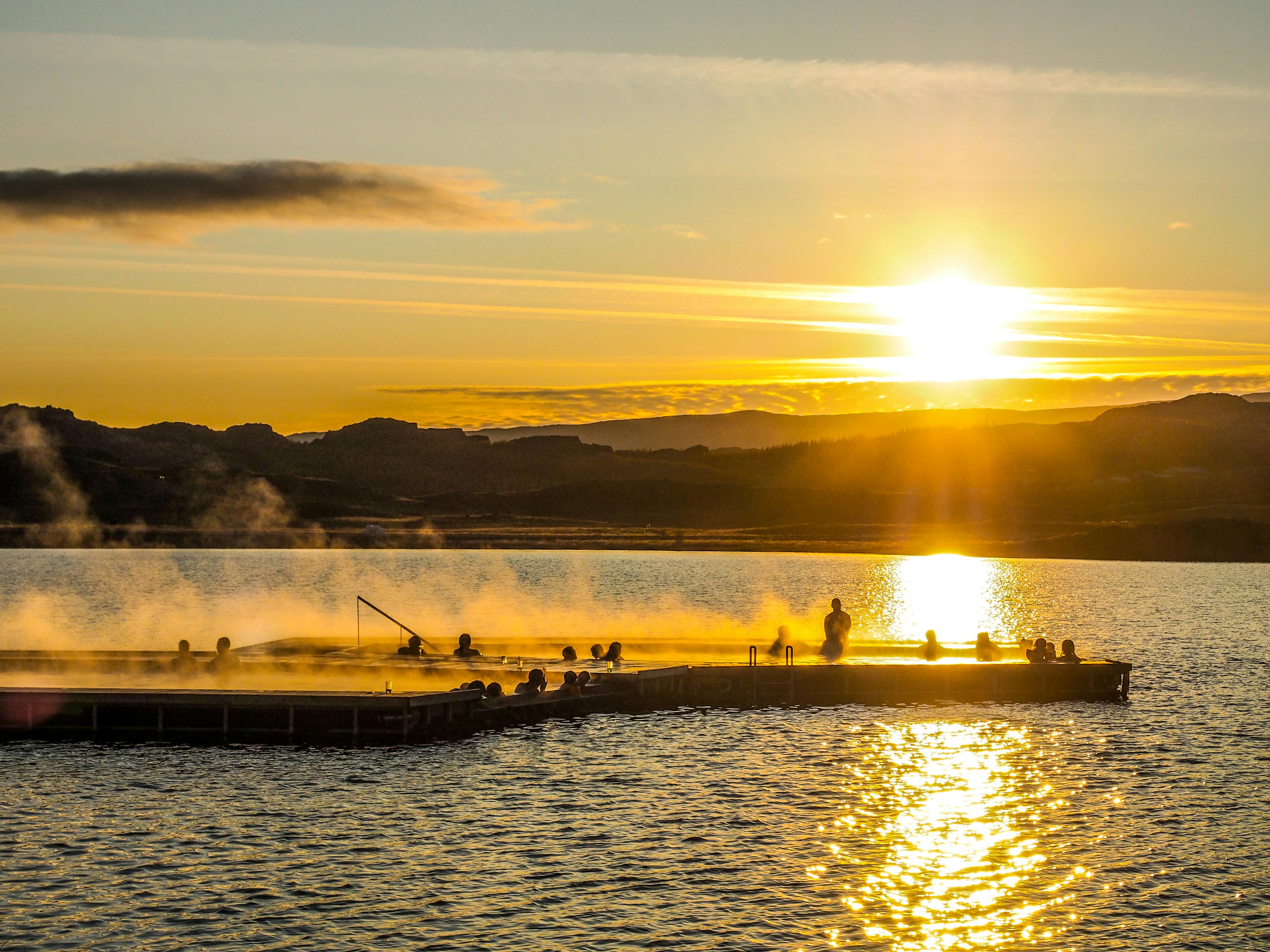 日落时分，人们可以在热气腾腾的温泉池中放松身心，周围有山脉和湖泊。
