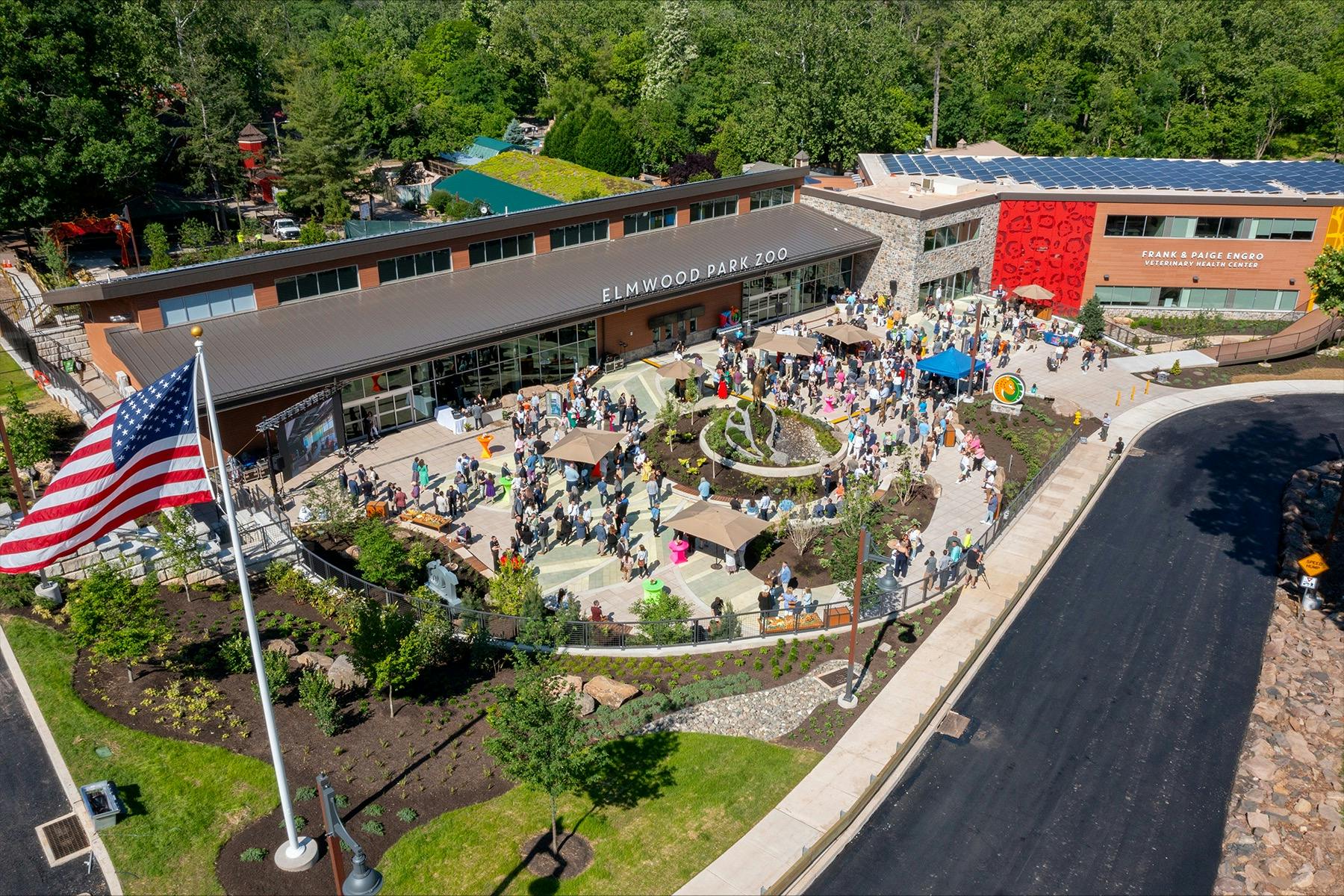 Aerial view of Elmwood Park Zoo entrance with a crowd of people gathered around a landscaped area on a sunny day.