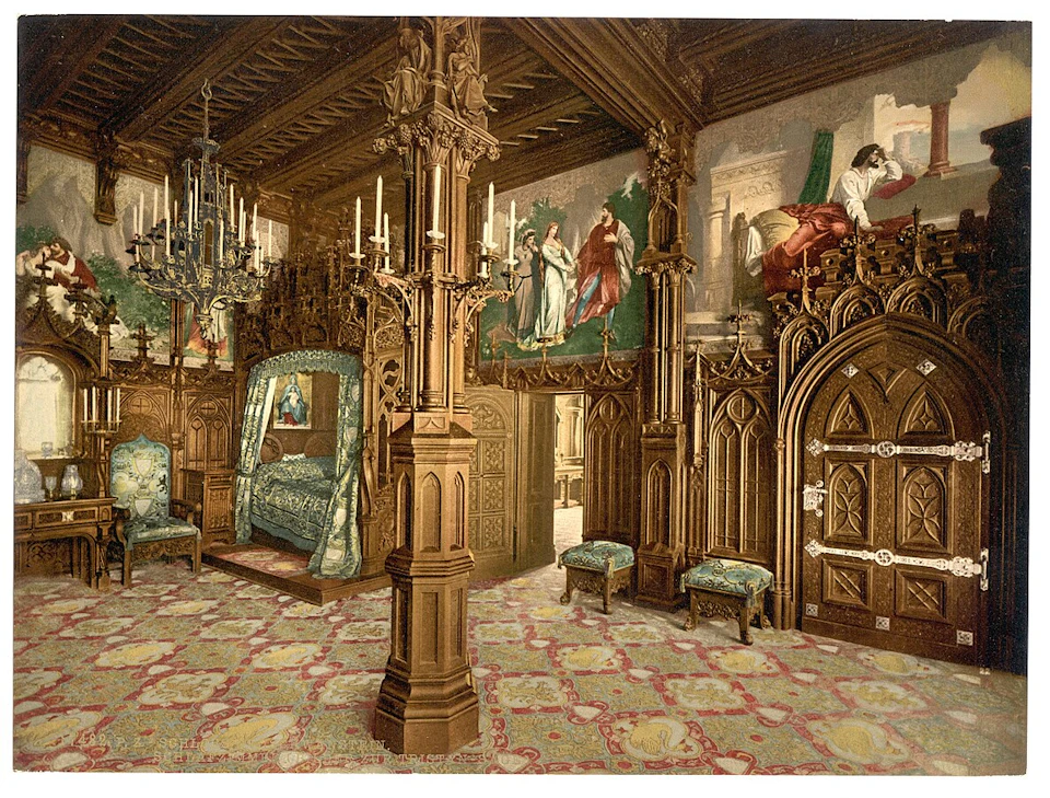 An ornately decorated room with wooden pillars, chandeliers, a canopy bed, ornate doors, upholstered chairs, and wall murals.