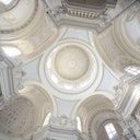 Un soffitto a cupola ornato di bianco e beige con finestre ad arco che lasciano entrare la luce naturale.