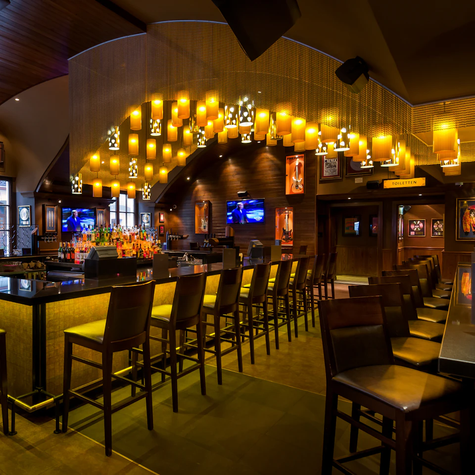 A bar with hanging yellow lanterns, high chairs at the counter, and television screens on the walls.