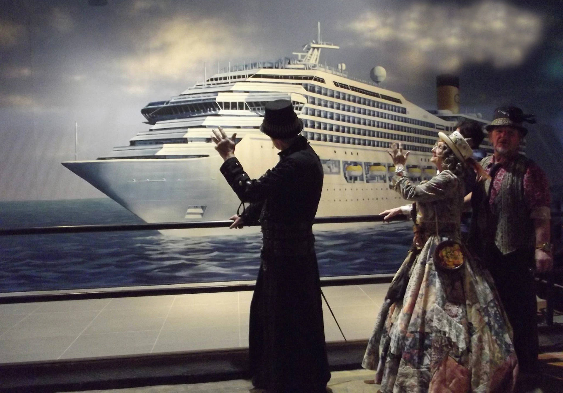 Two people in period costumes gesturing towards a large cruise ship depicted in a mural behind them.