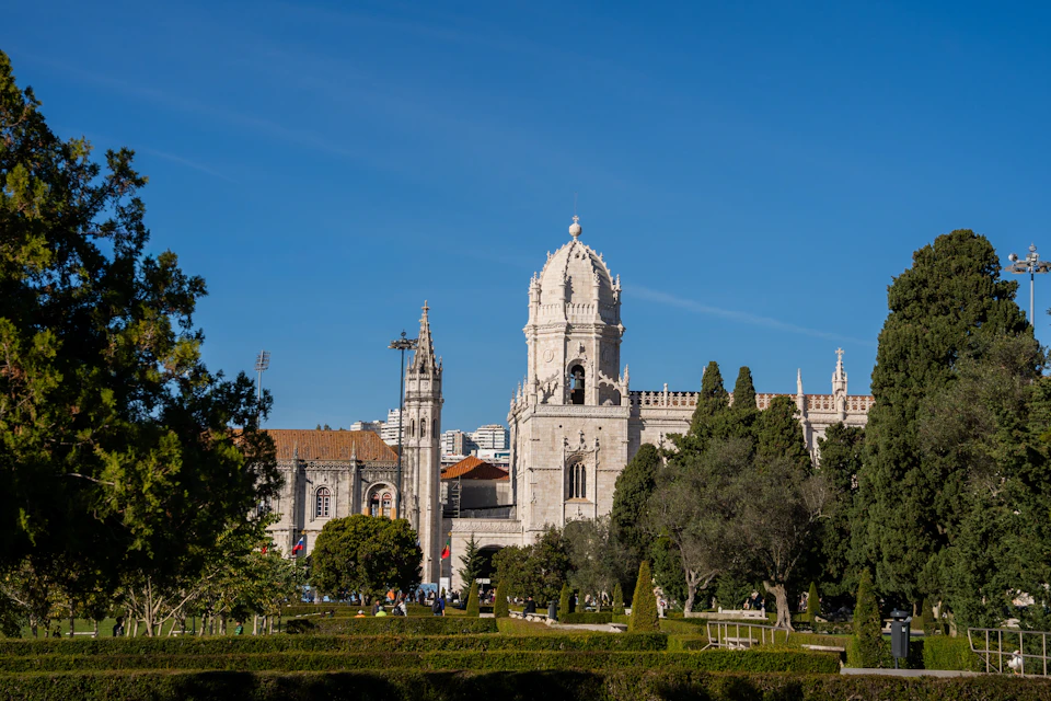 A historic building with ornate towers surrounded by a lush garden under a clear blue sky.