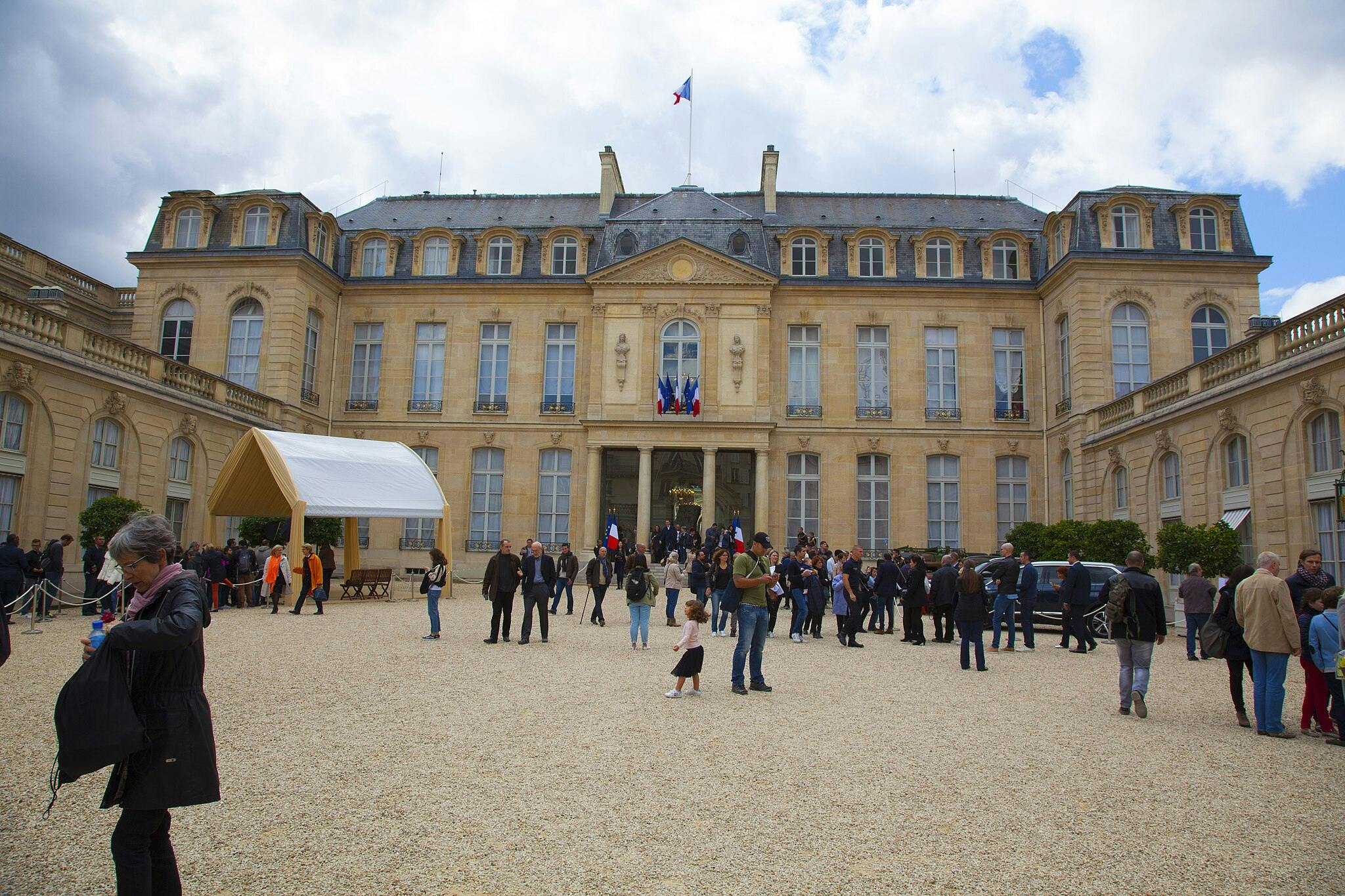 지붕에 커다란 창문 몇 개와 프랑스 국기가 있는 웅장하고 유서 깊은 건물 앞에 군중이 모여듭니다.