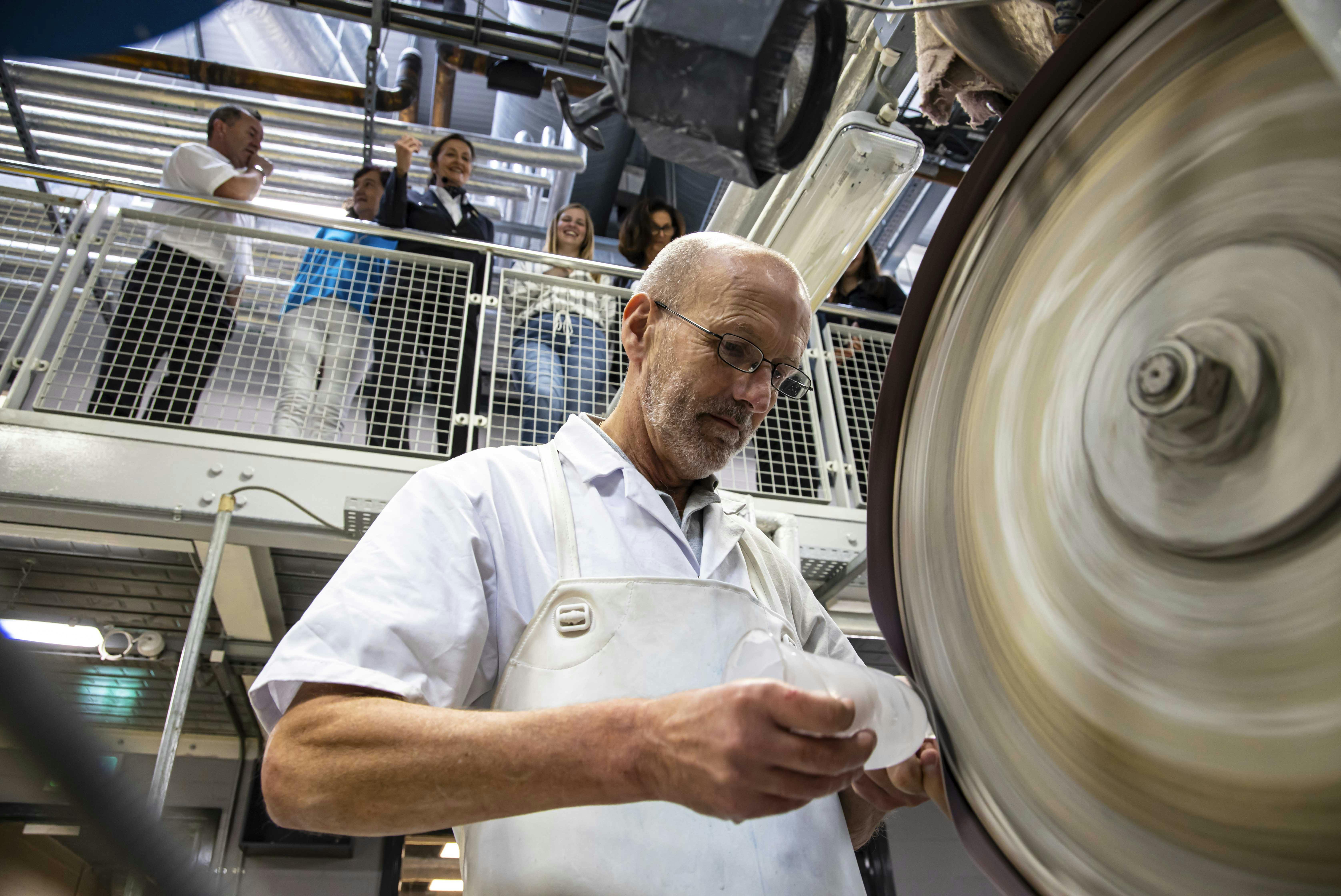 身穿白色外套的秃头男子与机器一起工作，而一群人则从上面的阳台上观察。