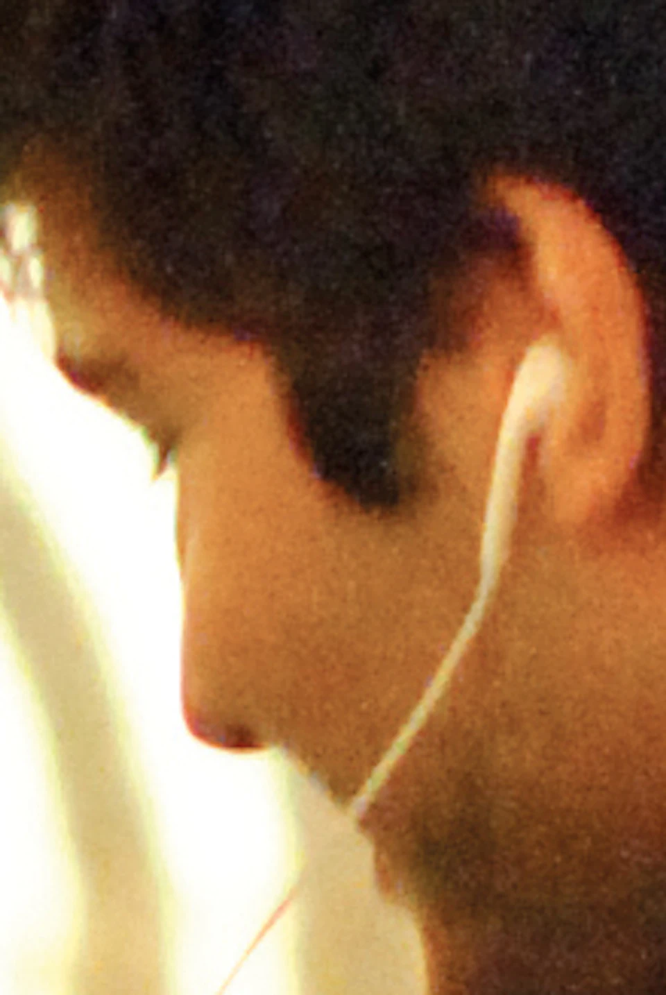 Two people, one wearing a white patterned shirt and the other in a dark jacket, share earphones while looking at a phone in a wine cellar.