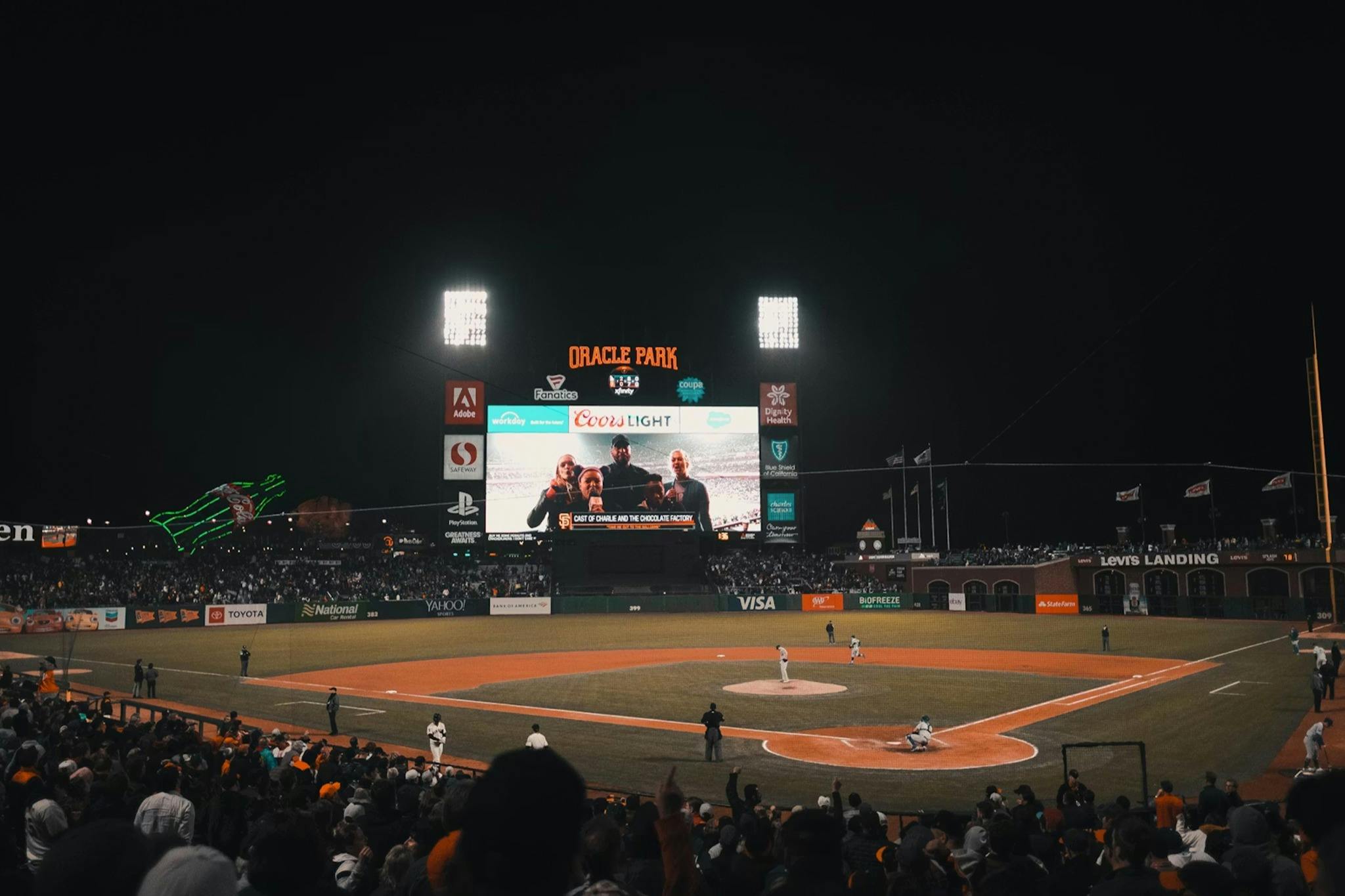 Noční baseballový zápas v Oracle Parku s rozsvícenou výsledkovou tabulí a diváky na tribunách.