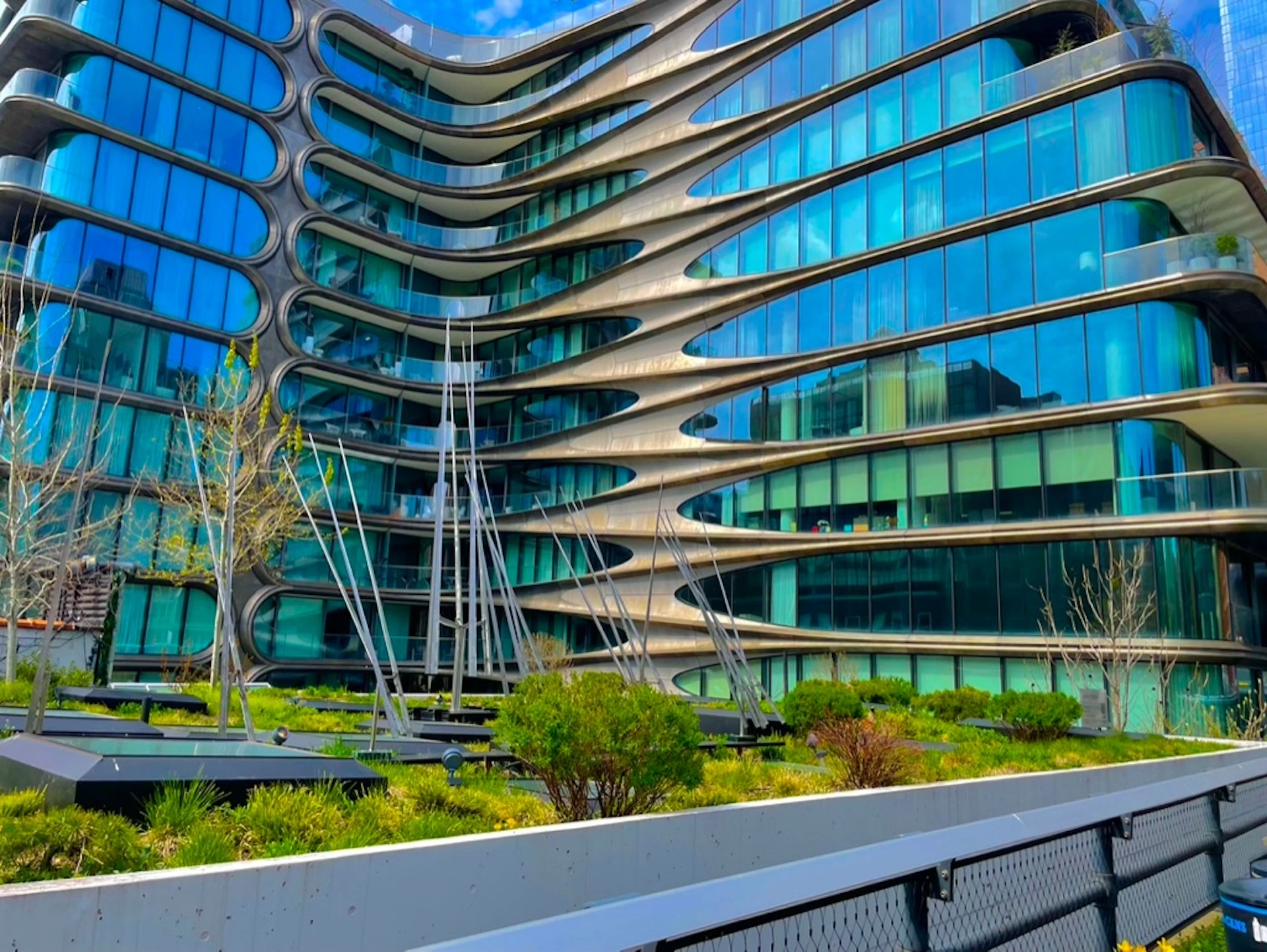 A modern building with curved geometric architecture, large glass windows, and landscaped greenery in the foreground.