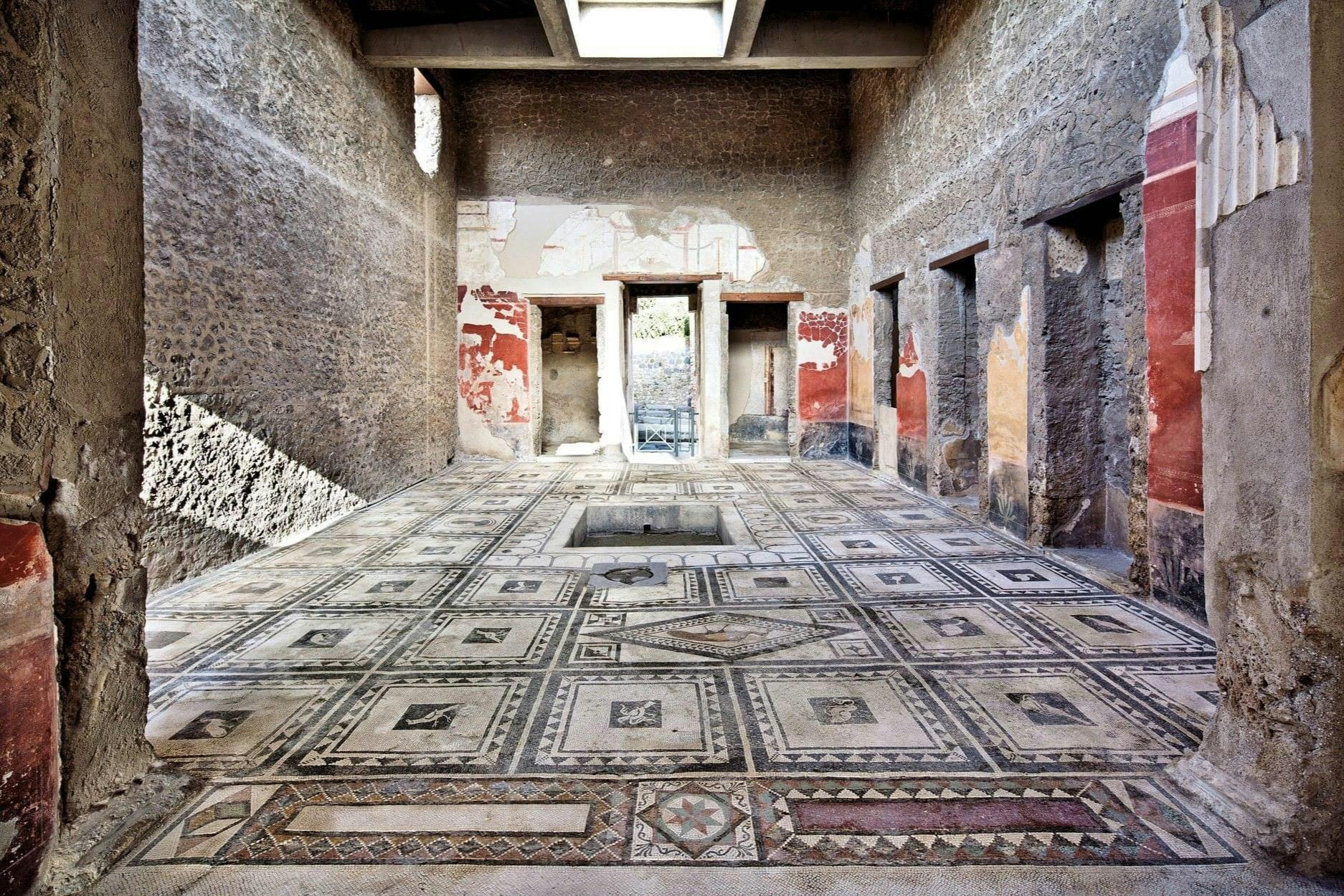 Ancient room with a detailed mosaic floor, ruined walls with fading frescoes, and multiple doorways leading to another area.