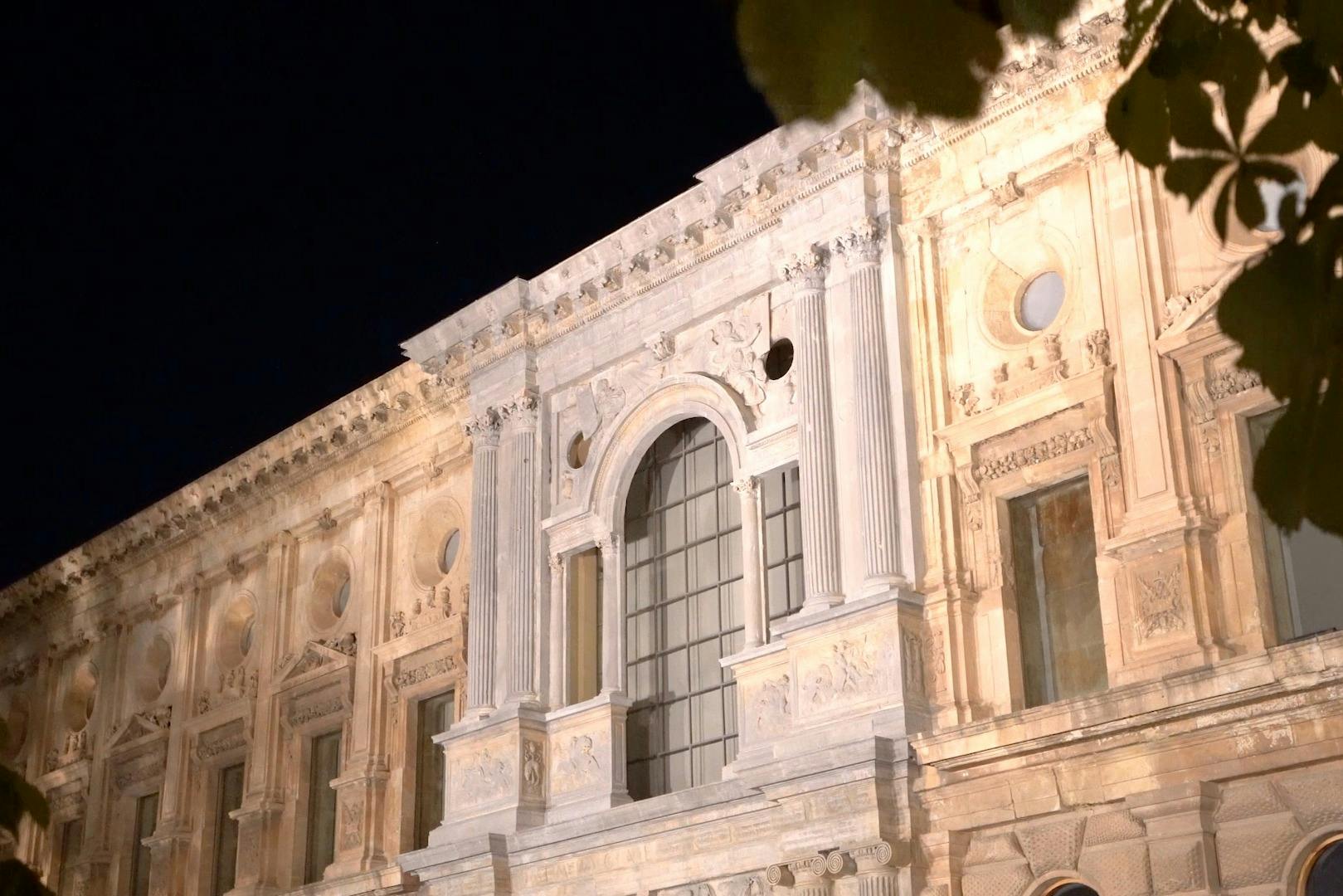 커다란 아치형 창문과 밤의 디테일한 조각이 있는 화려하고 빛나는 석조 건물 외관.