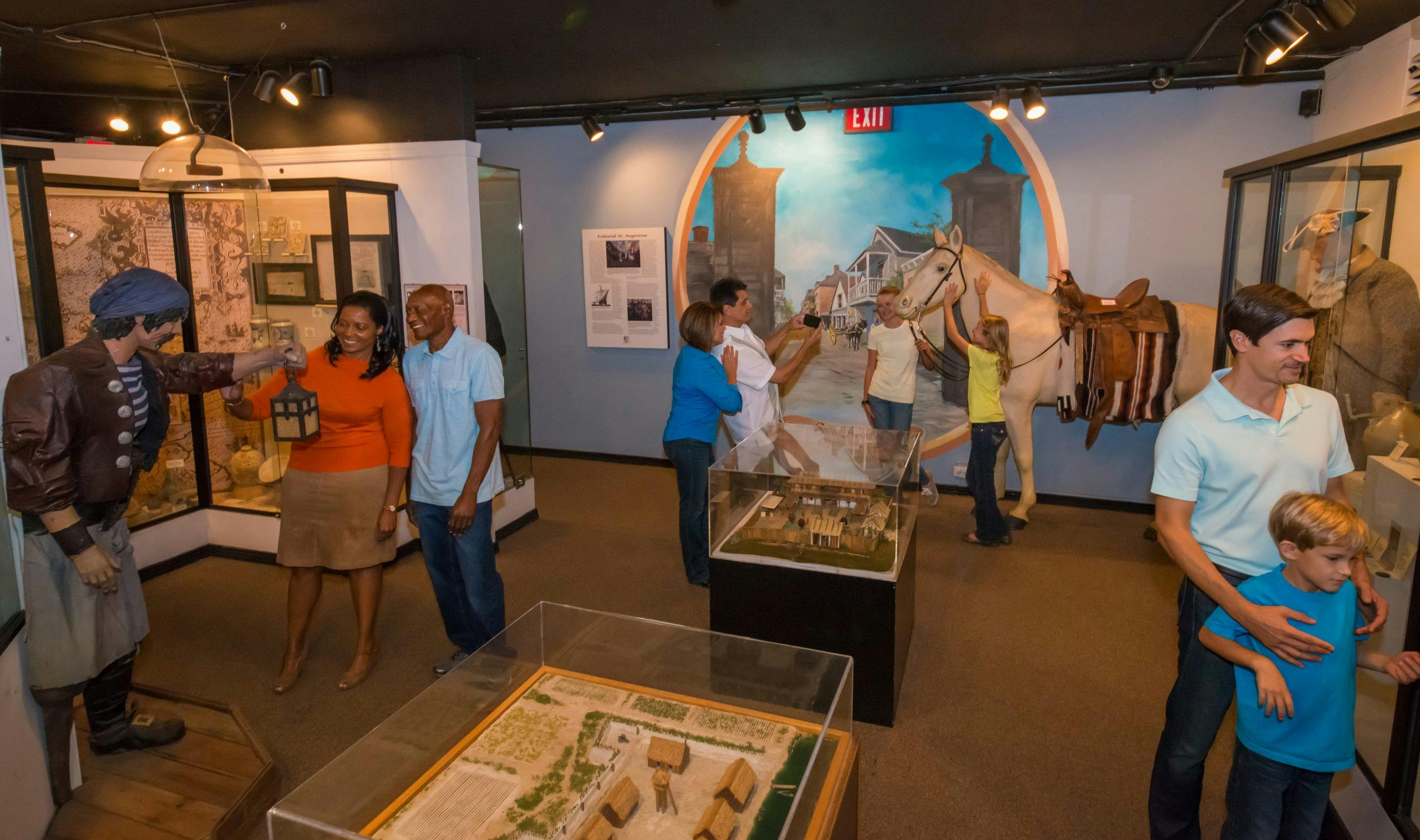 People exploring a museum exhibit featuring a life-sized horse model, historical displays, and architectural models.