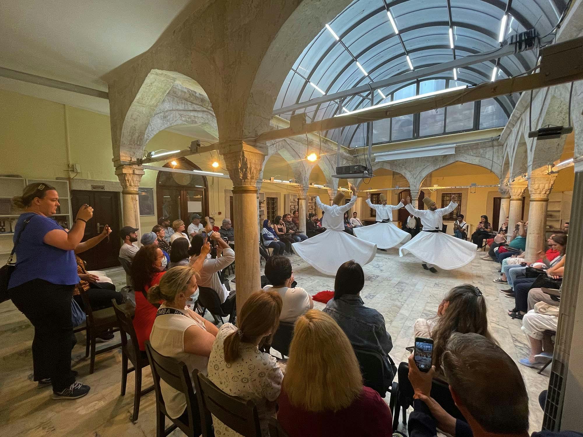 大厅里的人们观看和录制旋转的苦行僧表演。 房间有拱形柱子和玻璃天花板。
