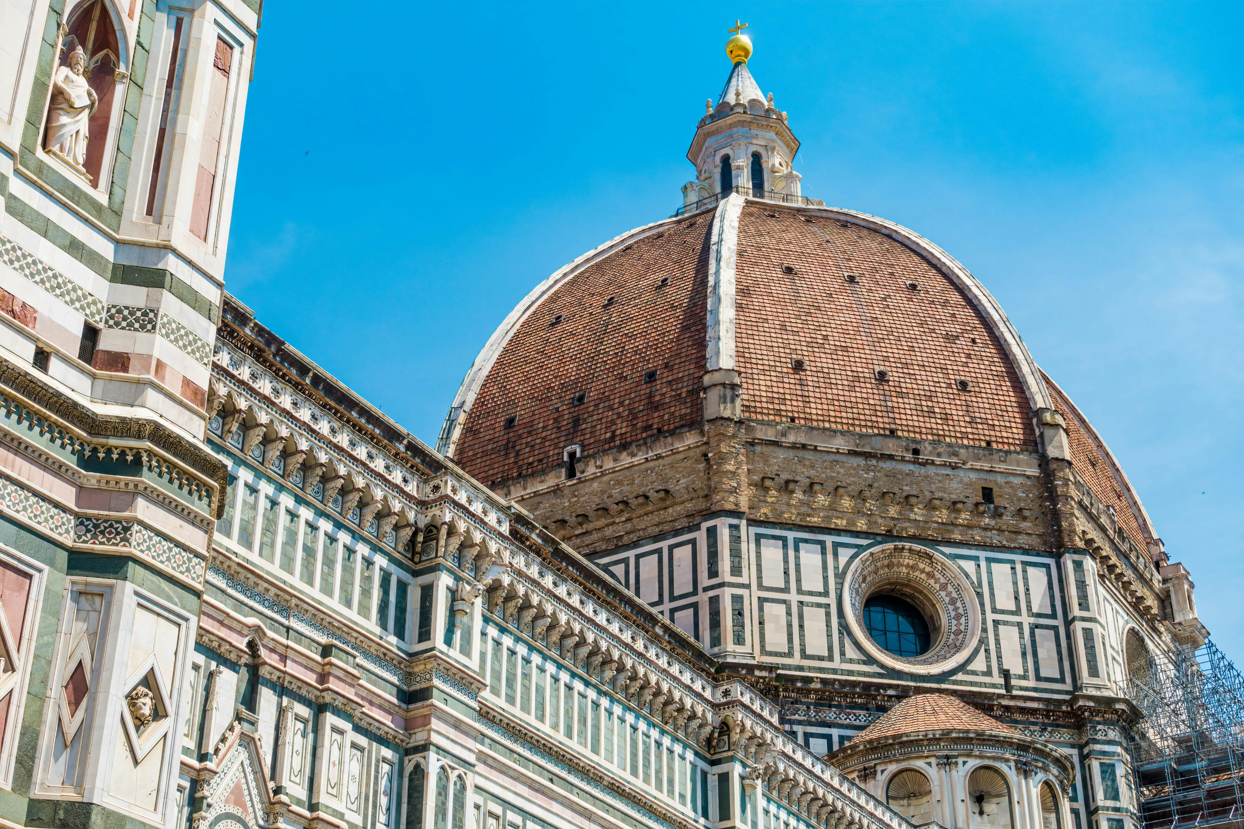 Close-up of Florence's Duomo with its intricate façade, detailed stonework, and large red-tiled dome against a clear blue sky.