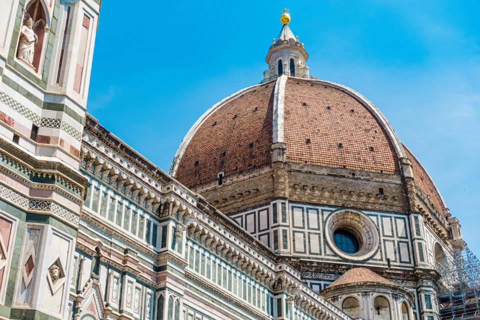 Close-up of Florence's Duomo with its intricate façade, detailed stonework, and large red-tiled dome against a clear blue sky.