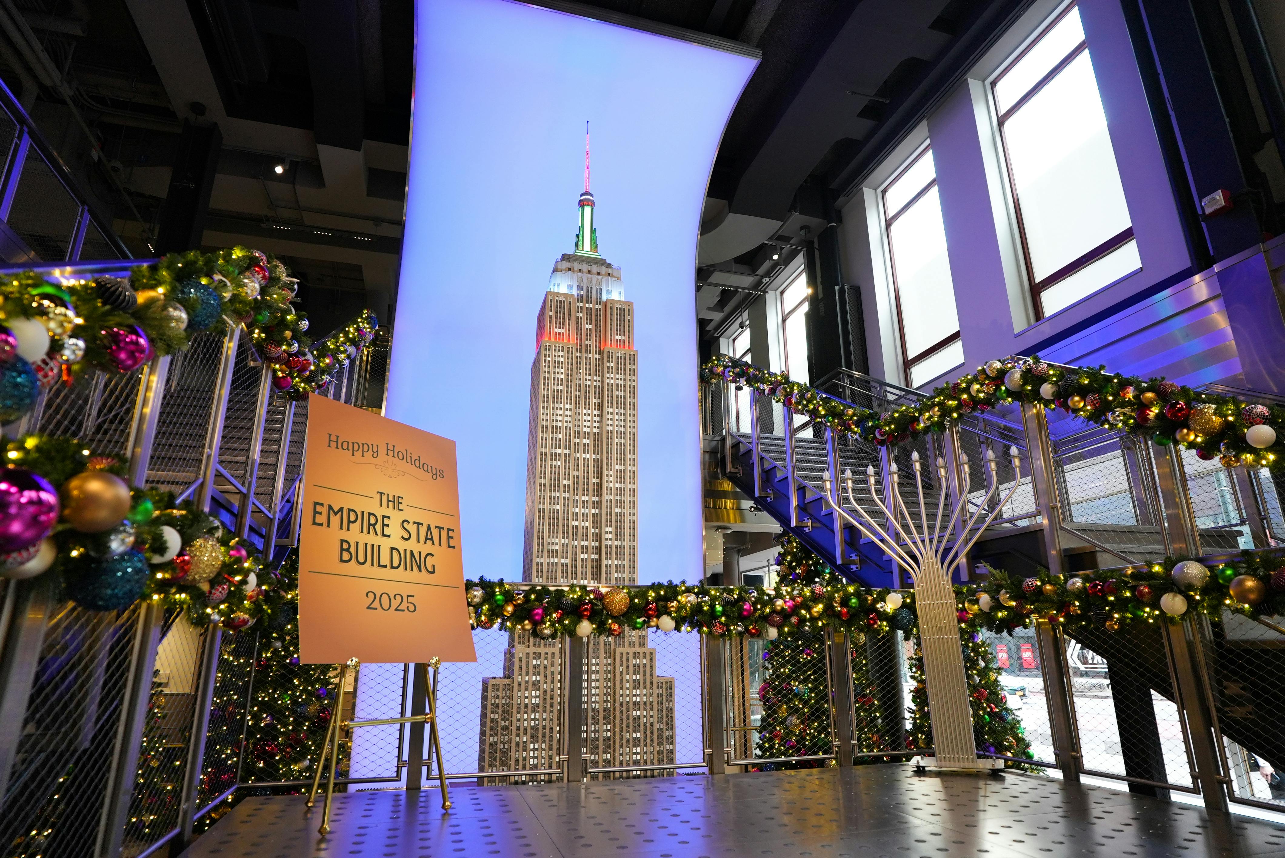 Et dekoreret interiør med feriekranse og en oplyst udstilling af Empire State Building. På et skilt står der "Happy Holidays 2025".