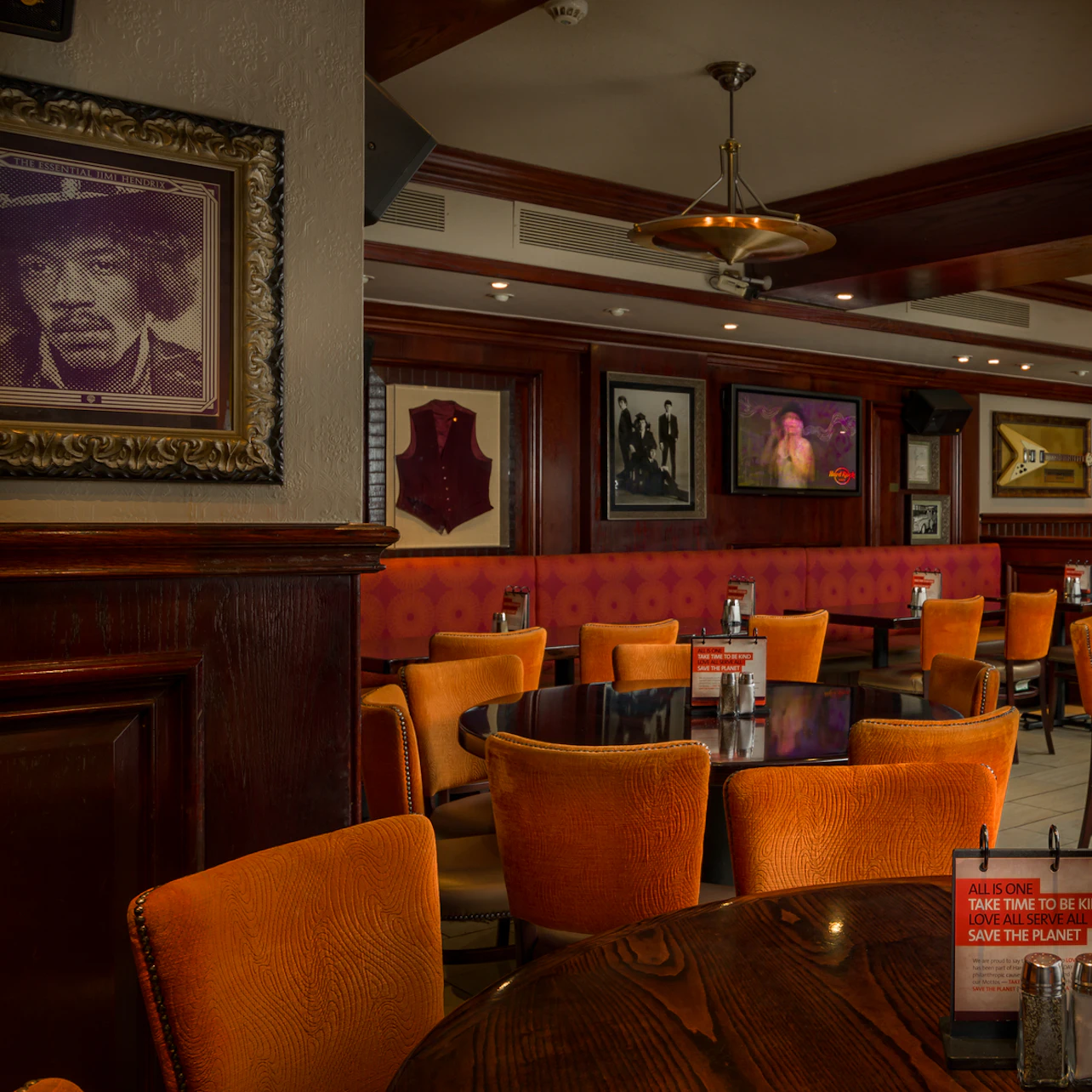 Restaurant interior with orange chairs, wooden tables, framed photos on the walls, and menus placed on tables.