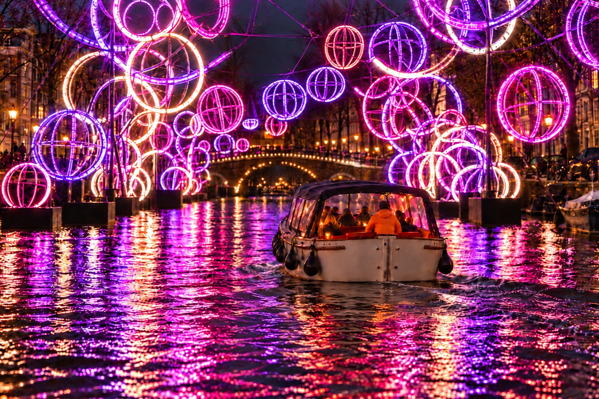 A canal boat navigates a waterway illuminated by colorful, glowing spherical light installations at night.
