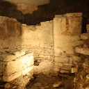 Ancient stone ruins with partial walls, rubble on the ground, and faint red markings on one wall.