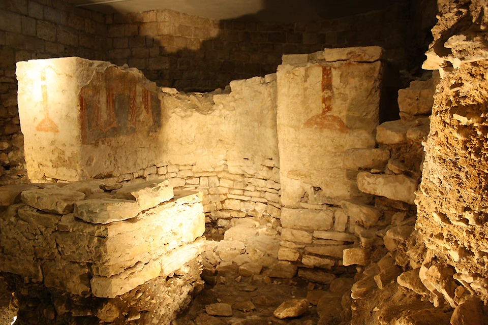 Ancient stone ruins with partial walls, rubble on the ground, and faint red markings on one wall.