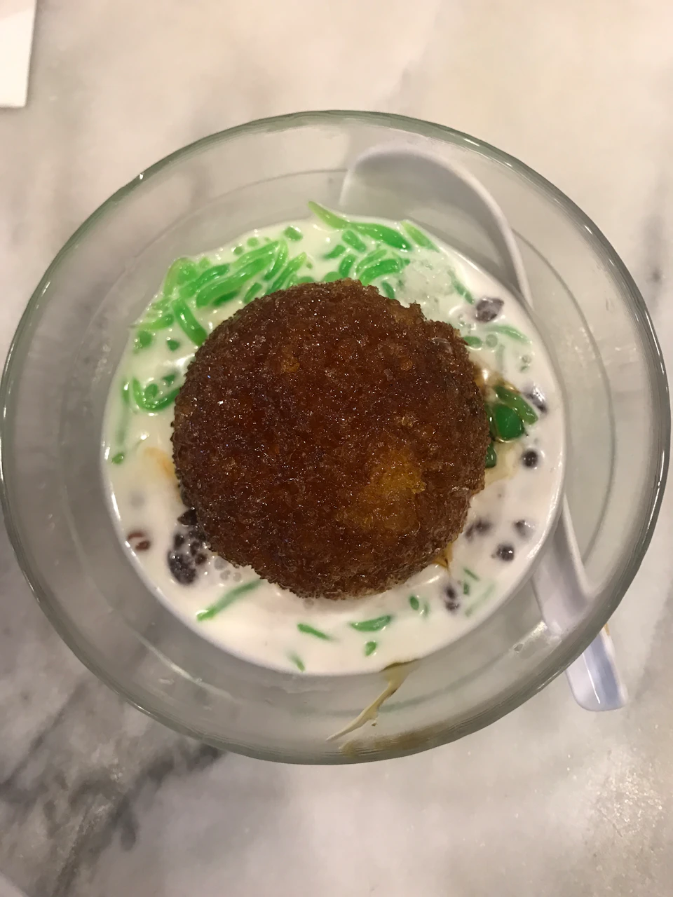 A bowl with shaved ice, green jelly noodles, red beans, and coconut milk, with a spoon on the side.