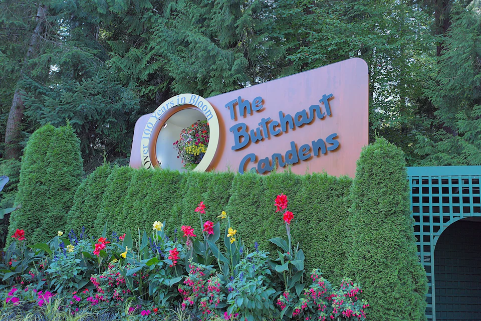 Sign for The Butchart Gardens surrounded by lush greenery and vibrant flowers, with text reading “Over 100 Years in Bloom.”