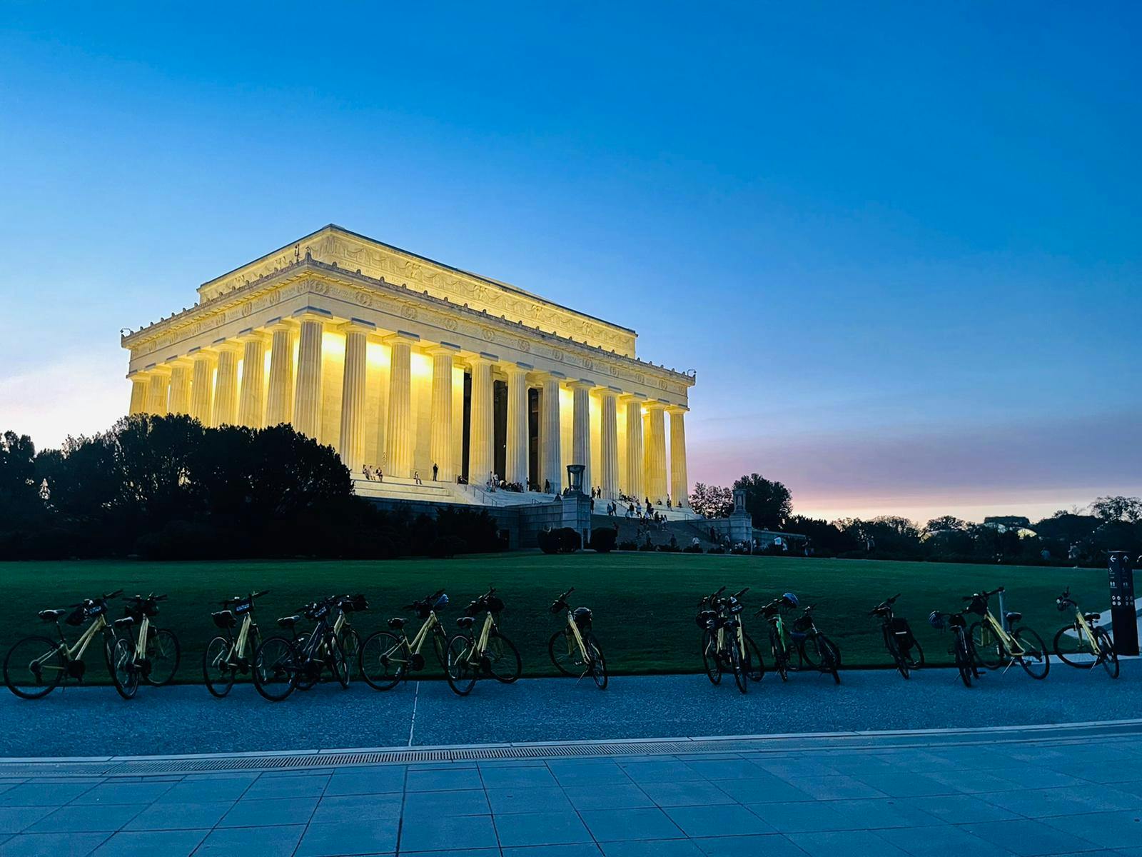 Illuminated Lincoln Memorial at dusk with bicycles lined up in the foreground and a clear evening sky.