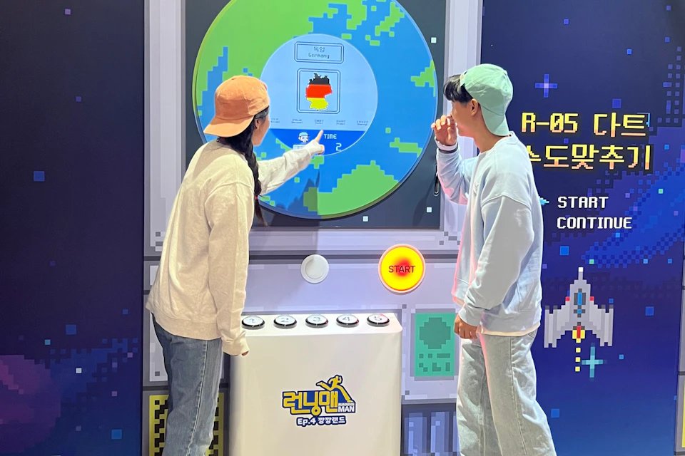 Two people interact with a large, colorful display featuring a pixelated world map and buttons. One points to the screen.