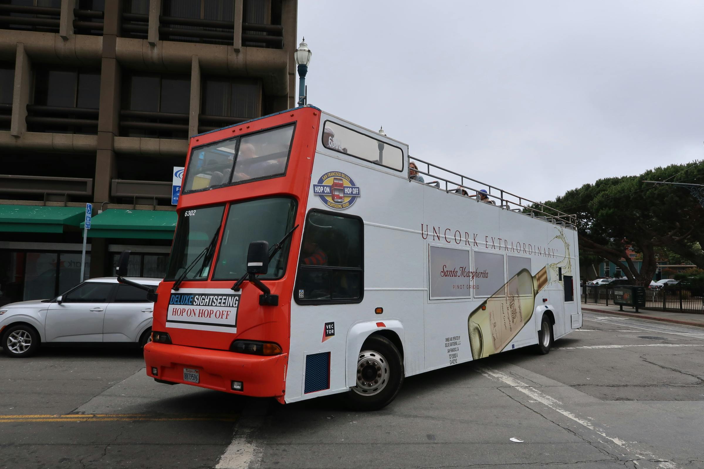 Bus touristique à impériale avec une publicité pour le vin "Uncork Extraordinary", stationné dans une rue de la ville près d'un bâtiment.