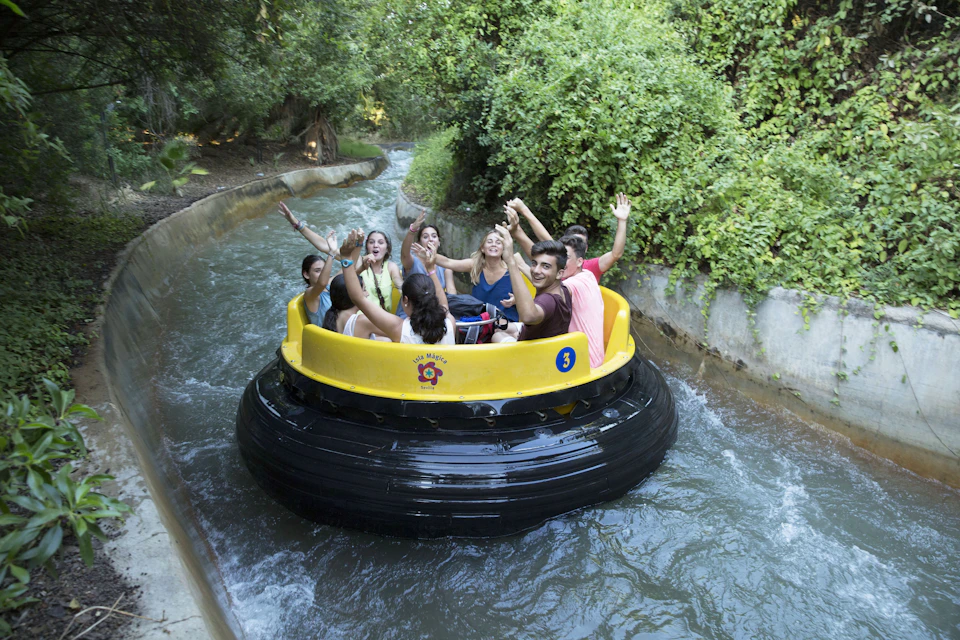 People joyfully riding a yellow raft on a water ride surrounded by lush green trees and foliage.