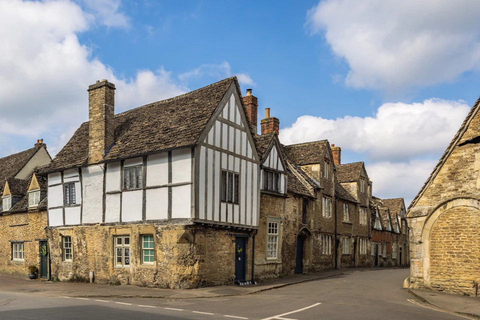 A row of historic stone buildings with timber-frame details on a street corner under a partly cloudy blue sky.