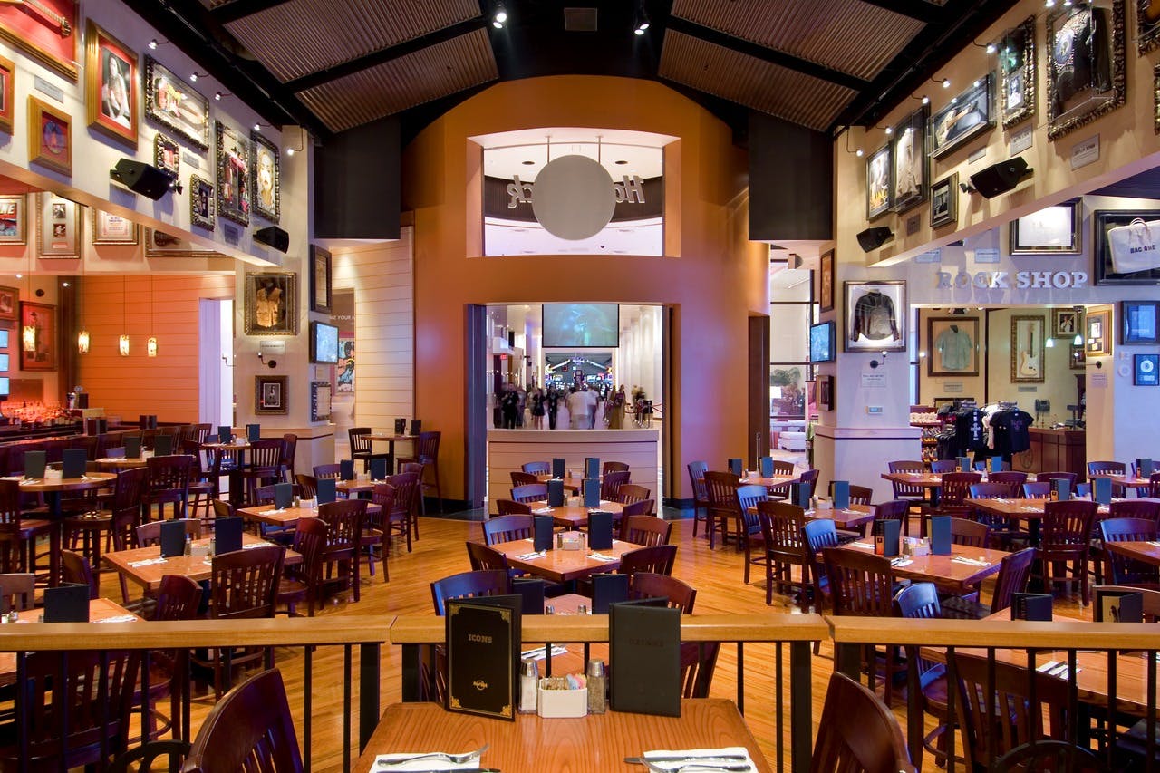 A spacious, modern restaurant with wooden tables and chairs, elegant decor, and picture frames on cream and orange walls.