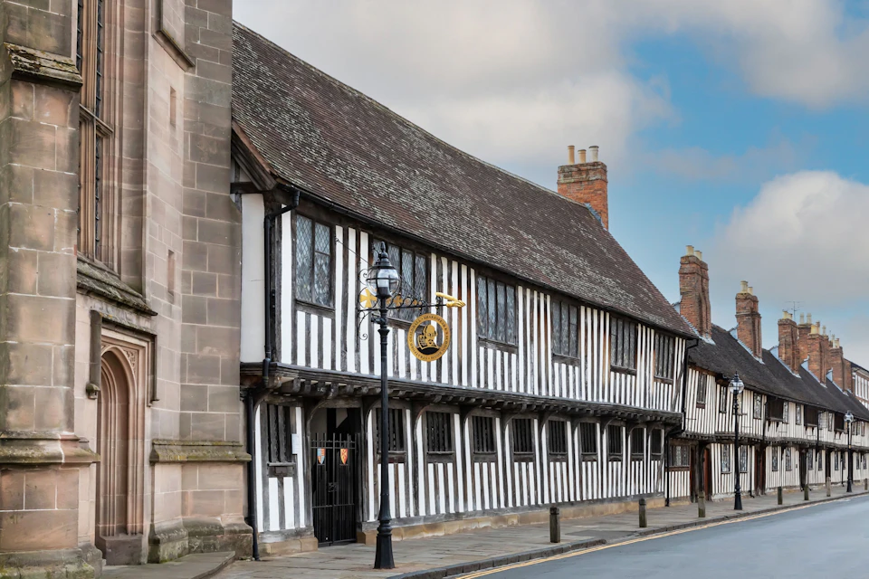 A historic black-and-white timber-framed building on a quiet street, with a hanging sign and a lamppost in front.