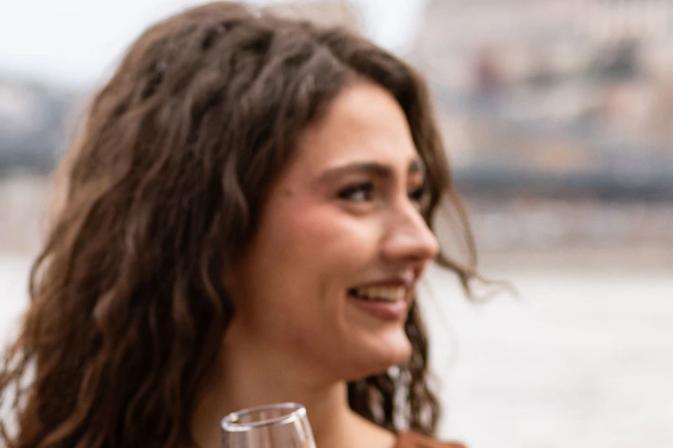 Two women smiling and holding glasses of champagne on a boat, with a bottle being poured in the foreground.
