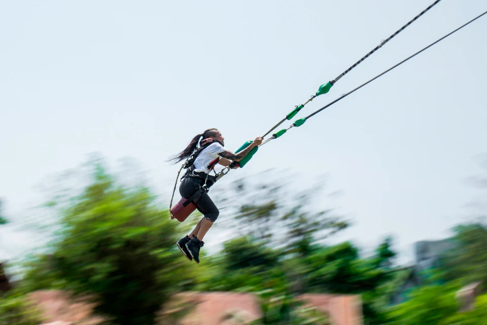 A person swinging on a harnessed bungee swing outdoors, with trees and a clear sky in the background.