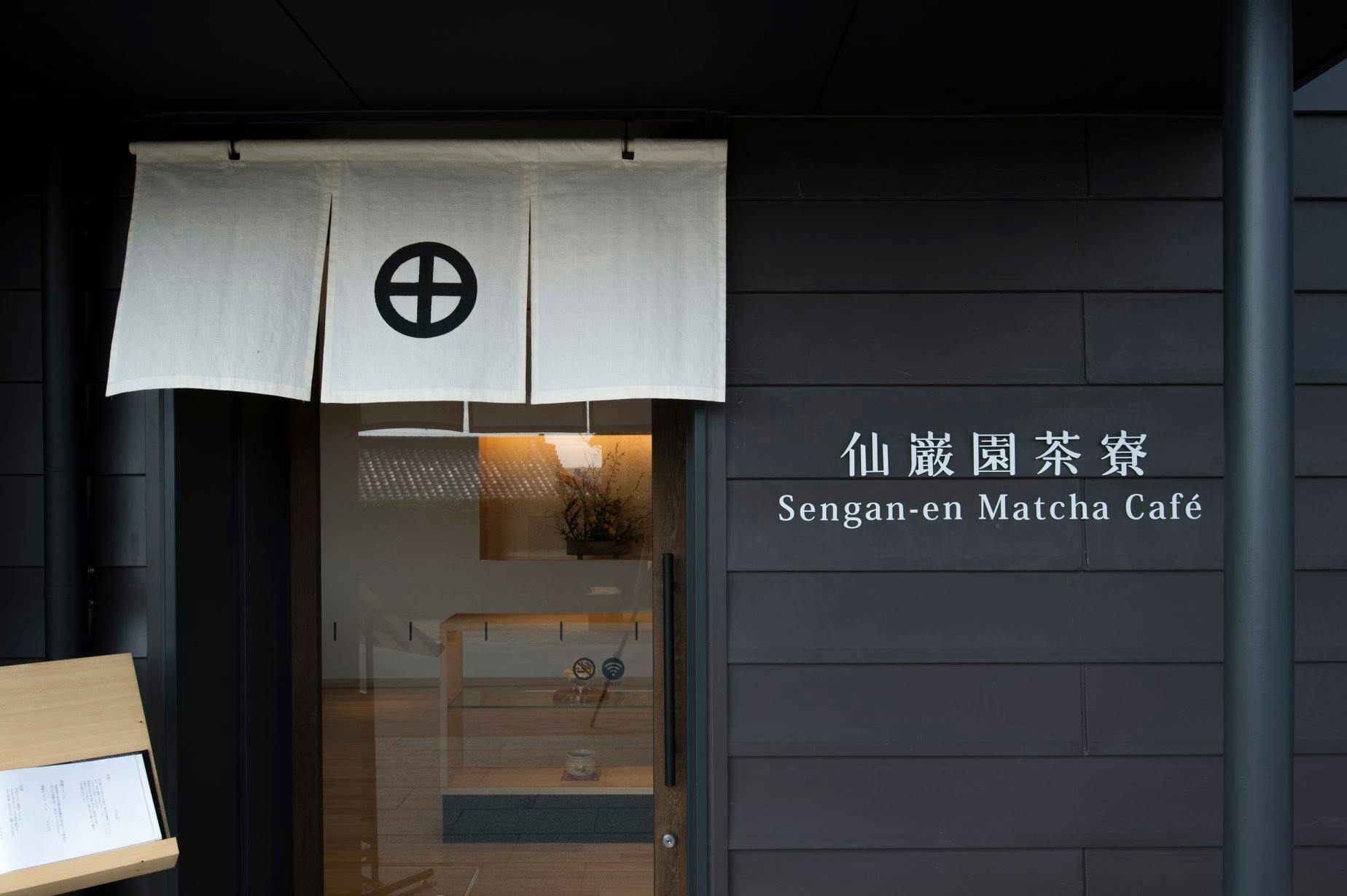 Entrance to Sengan-en Matcha, featuring a curtain with a circular design, signage, and a view of a minimalist interior.