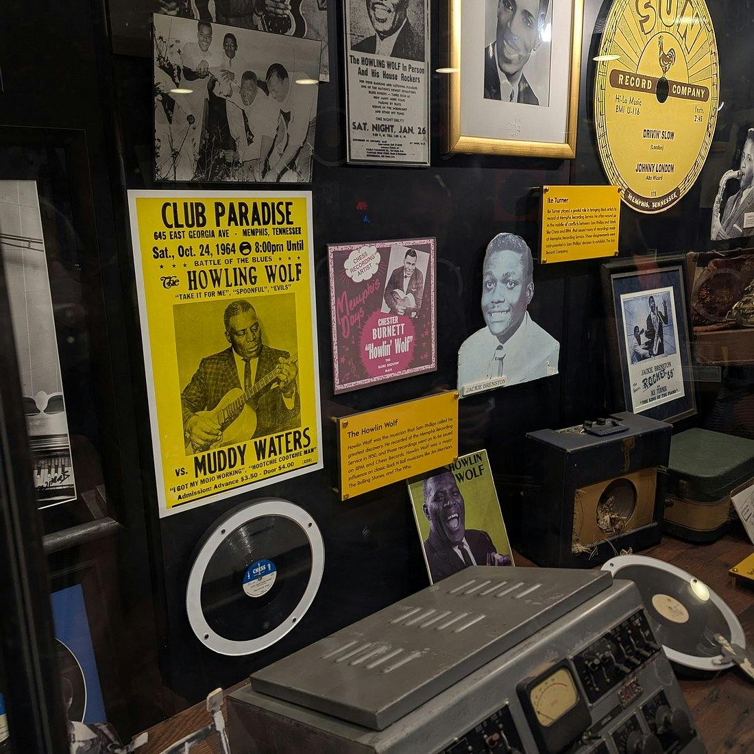 A display case showcasing vintage music memorabilia, including posters, photos, a record player, and vinyl records.