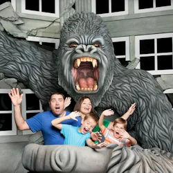 A family posing with a large gorilla statue, which appears to be breaking through a wall, in a fun and playful setting.