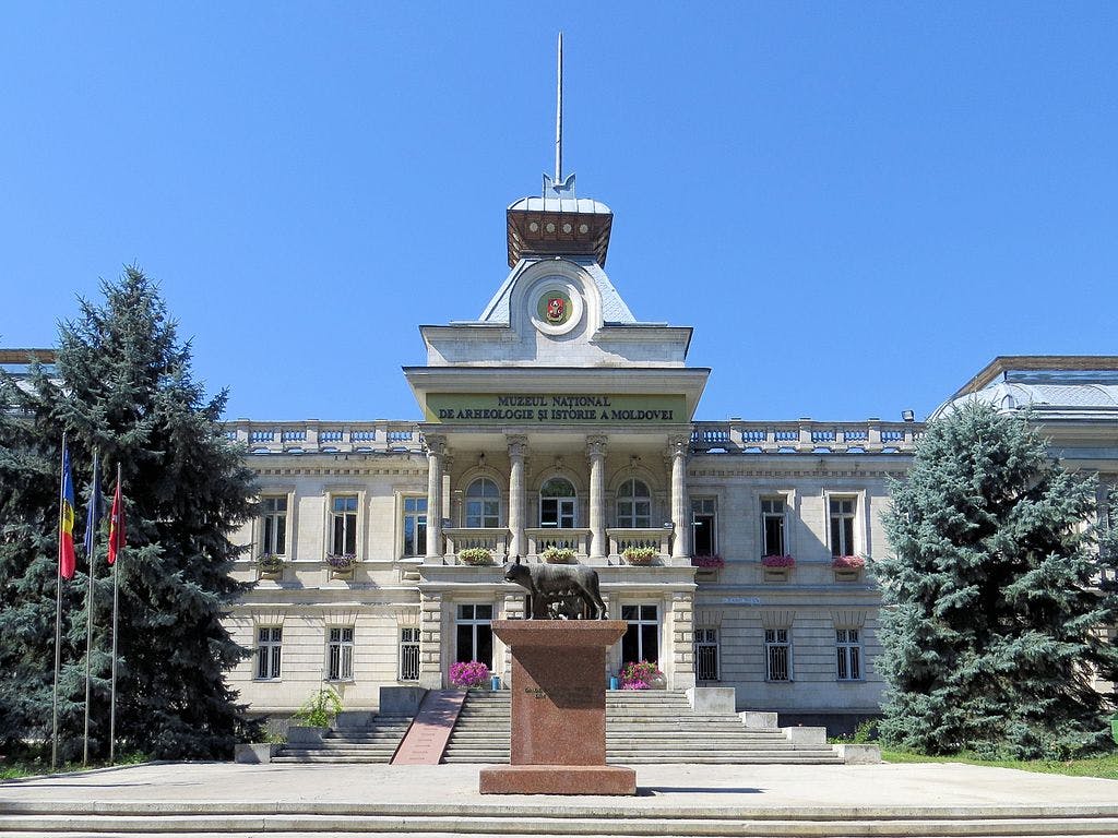 A grand building with columns, labeled "Muzeul Național de Arheologie și Istorie a Moldovei," flanked by trees, and displaying a statue on a pedestal.