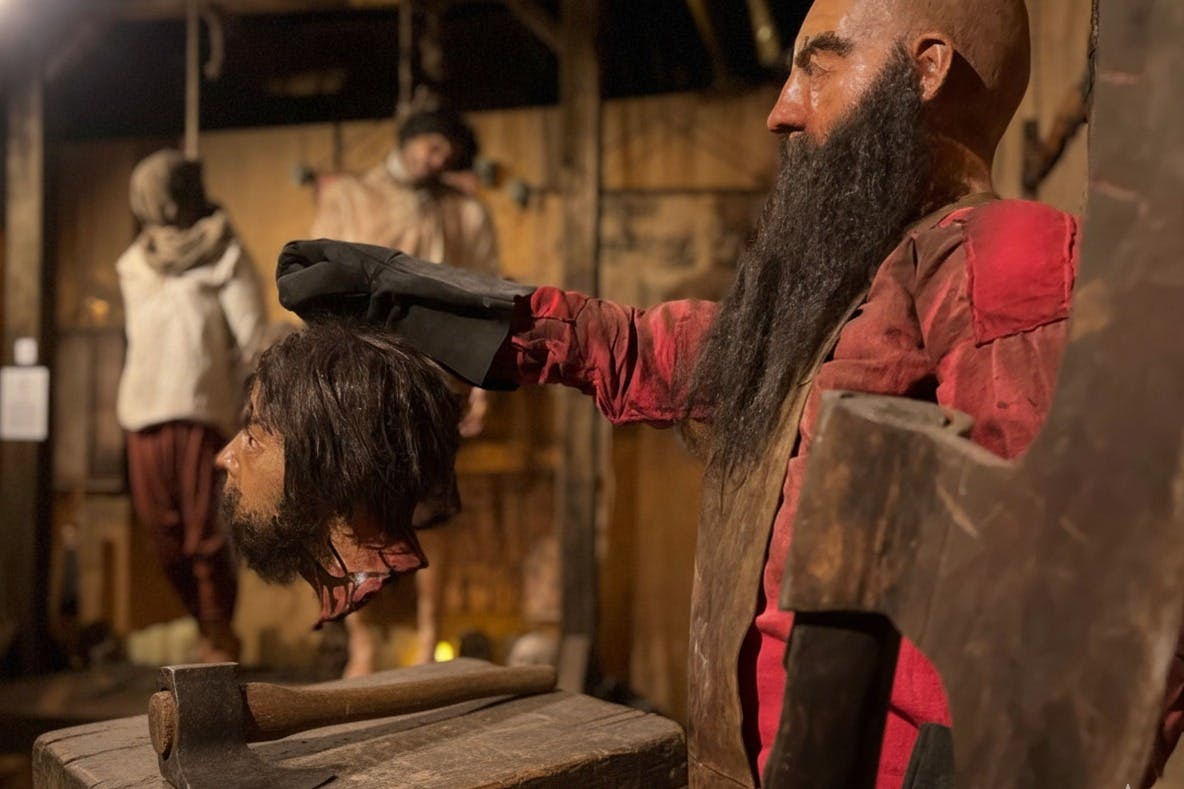 Манекен, одетый в красное с длинной бородой, держащий реквизит, часть исторической или тематической выставки с деревянным декором.