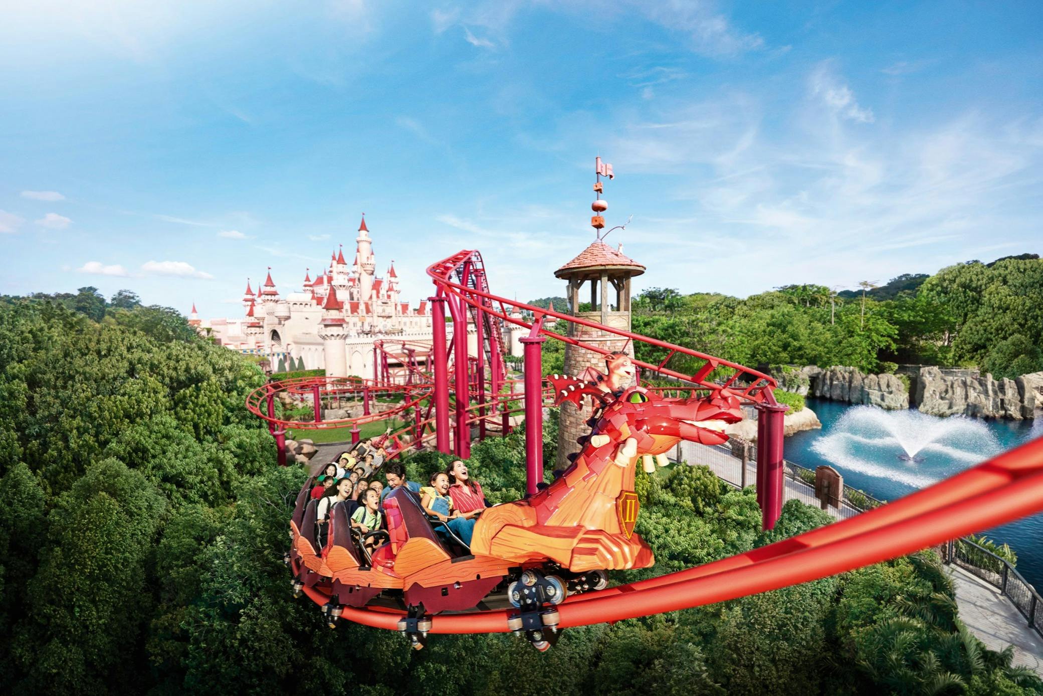 Uma montanha-russa com a forma de um dragão, com os passageiros a percorrerem um parque caprichoso com um castelo e vegetação.