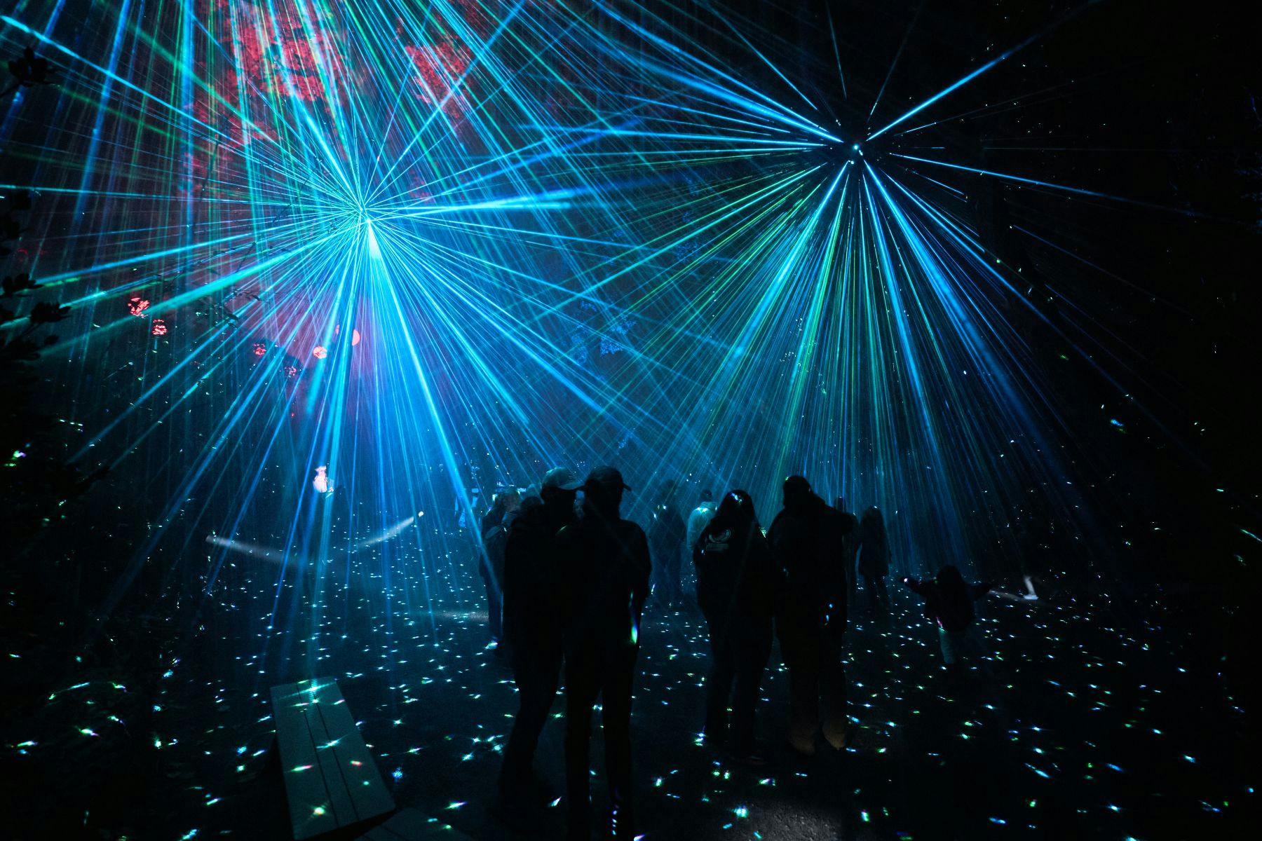 People standing under vibrant blue laser beams in a dark space, with light reflections on the ground.